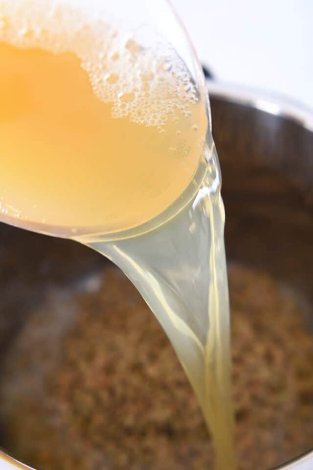 Pouring chicken broth into instant pot with dry lentils.