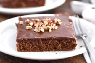 Square of frosted chocolate Texas sheet cake on white plate with pecans on top.