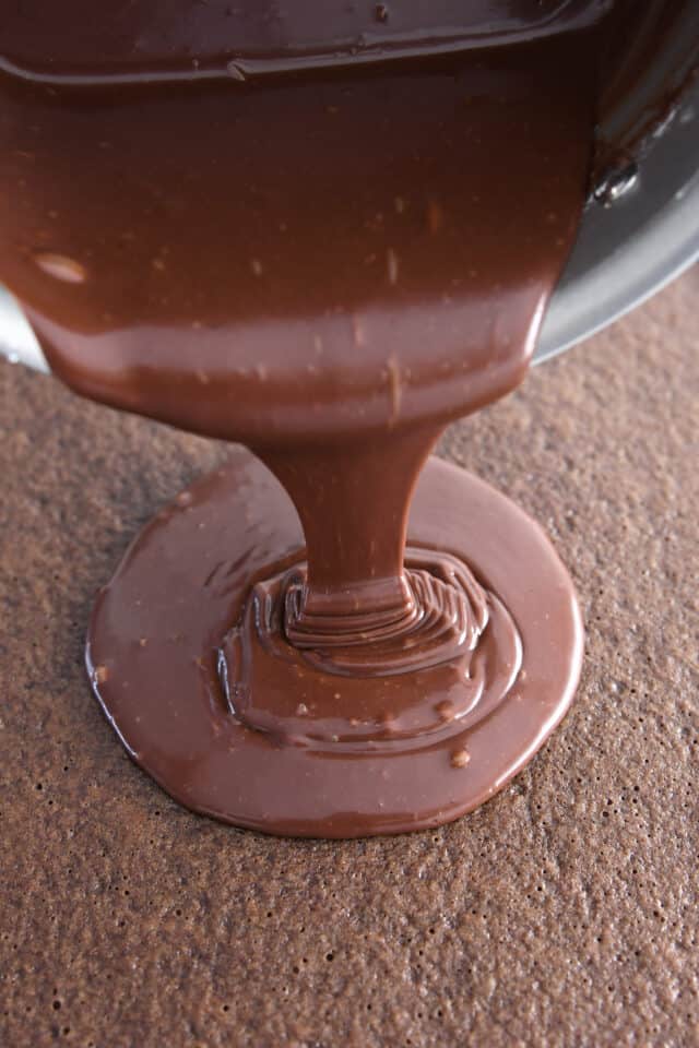 Pouring warm frosting over chocolate sheet cake.