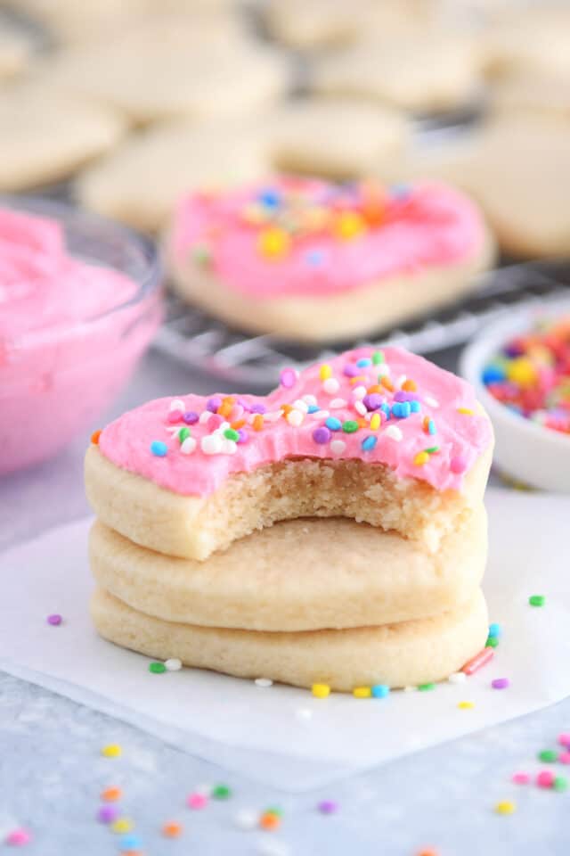 Bite taken out of pink frosted heart shaped sugar cookie stacked on two unfrosted cookies.