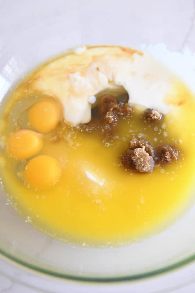 Melted butter, eggs, brown sugar, white sugar, and buttermilk in glass bowl.