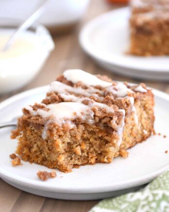 Bite taken out of carrot cake coffee cake on white plate with cream cheese drizzle.