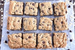 Twelve squares of cut chocolate chip cookie bars on white parchment paper.
