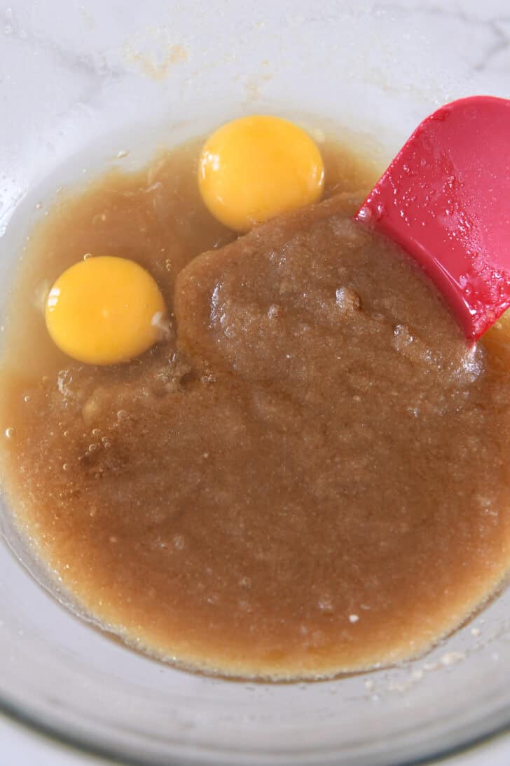 Eggs in sugary muffin batter in glass bowl.