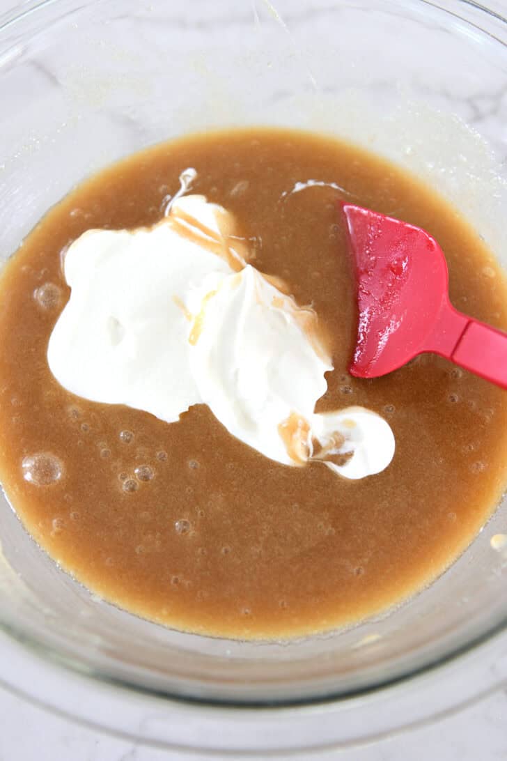 Sour cream added to muffin batter in glass bowl.