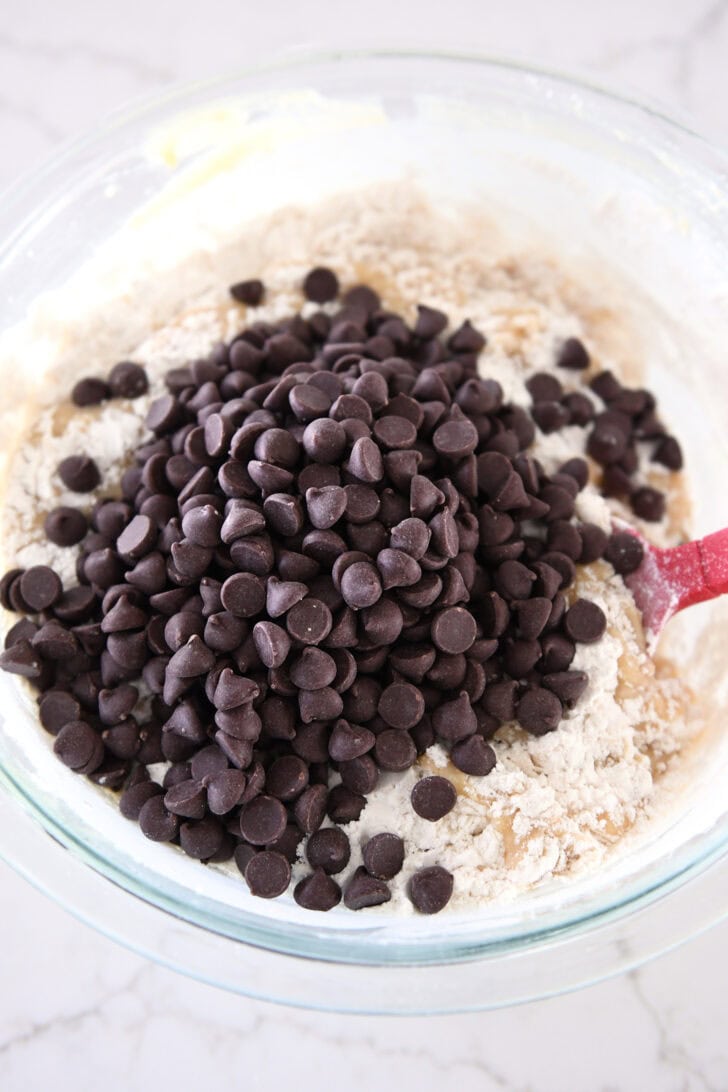 Chocolate chips on top of muffin batter in glass bowl.