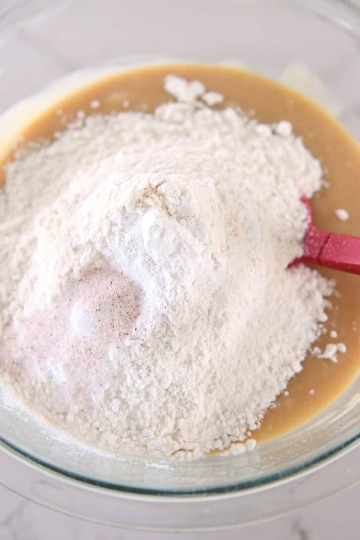 Flour, salt and baking soda in wet ingredients for muffin batter in glass bowl.