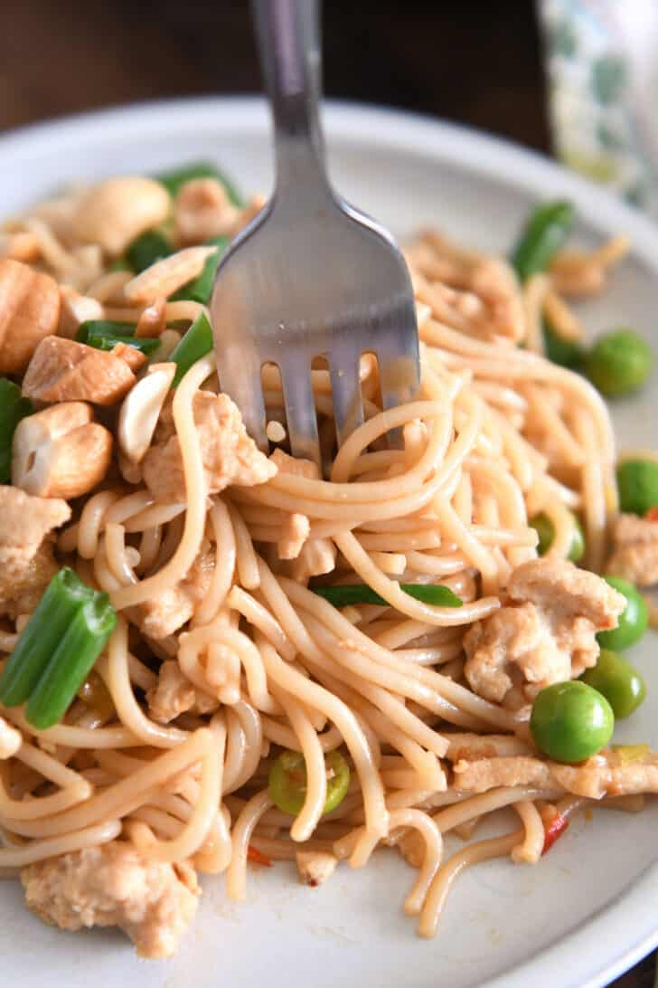 Fork twirling bite of ramen noodles with peas and green onions.