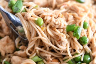 Tongs grabbing scoop of ramen noodles with peas and green onions.