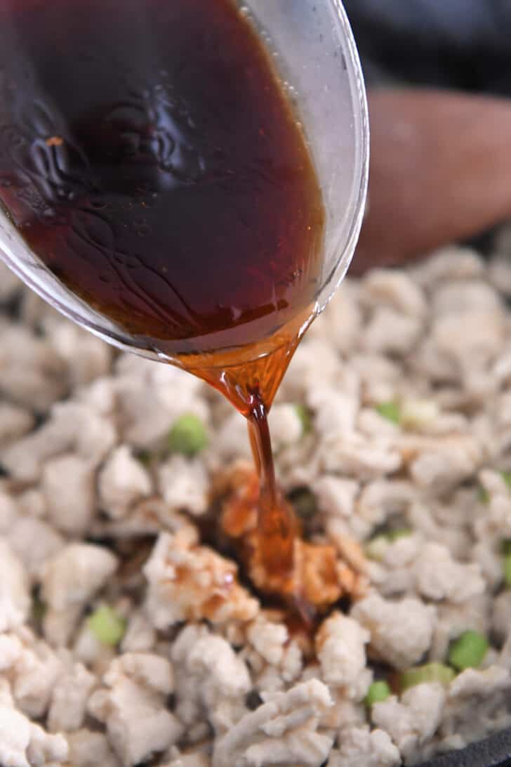 Pouring spicy garlic sauce into skillet with ground turkey.
