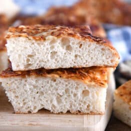 Two stacked pieces of fluffy Italian cheese bread on wood cutting board.