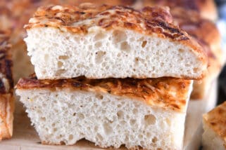 Two stacked pieces of fluffy Italian cheese bread on wood cutting board.