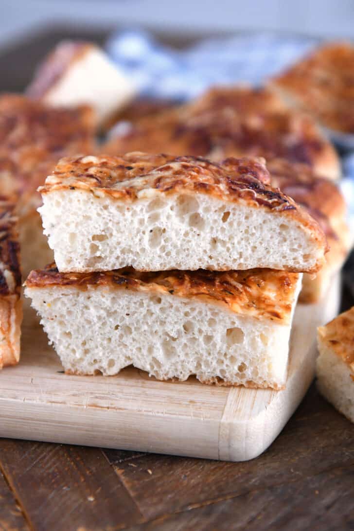 Two stacked pieces of fluffy Italian cheese bread on wood cutting board.