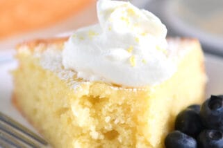 Triangle of olive oil cake on white plate with whipped cream and blueberries.