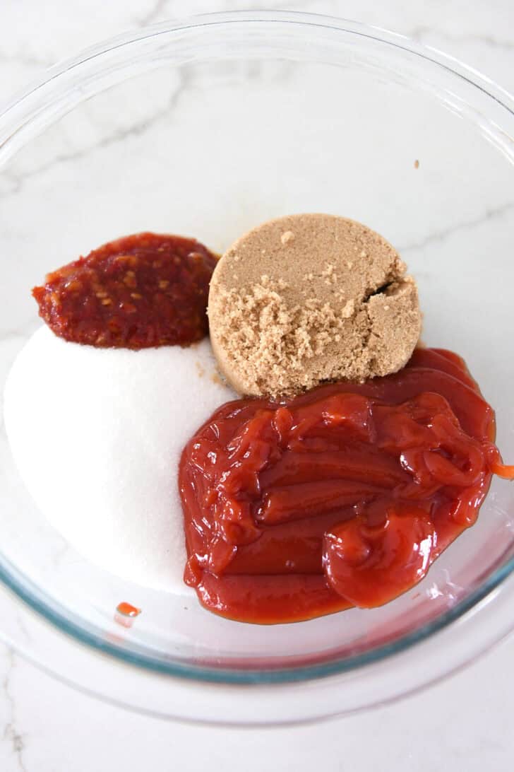 Glass bowl with sugar, ketchup, chili garlic sauce and brown sugar.