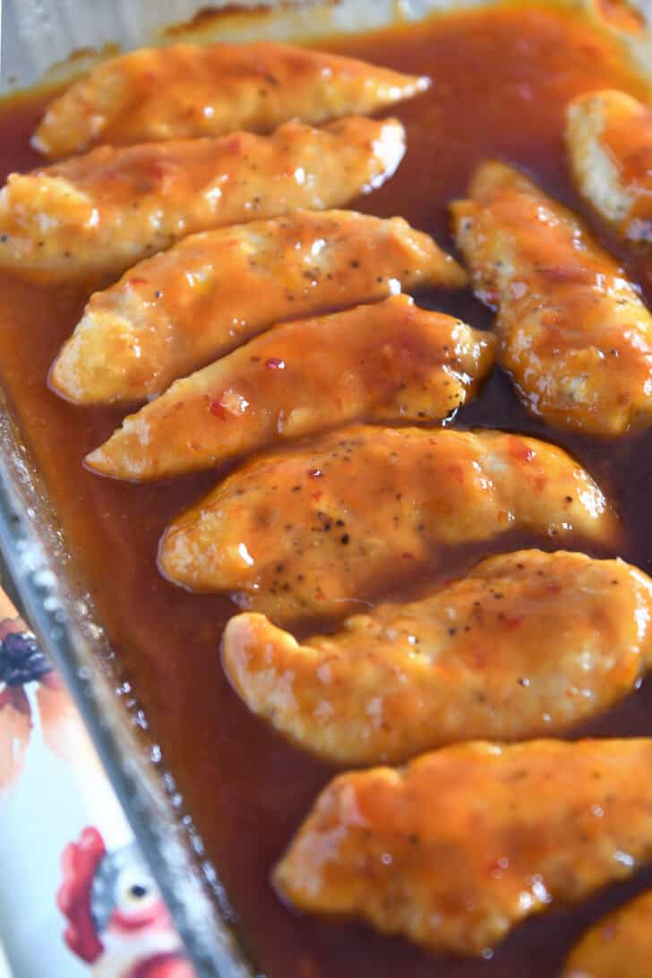 Glass baking dish with chicken tenders and chili garlic sauce.