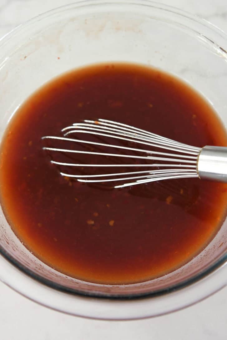 Glass bowl with chili garlic sauce and whisk.