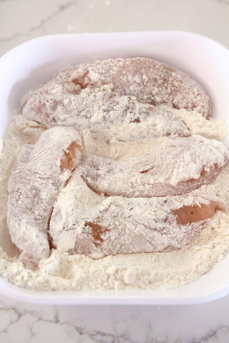 Chicken tenders tossed in bowl with flour.