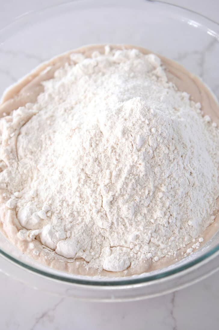 Flour added to yeast and water in glass bowl.