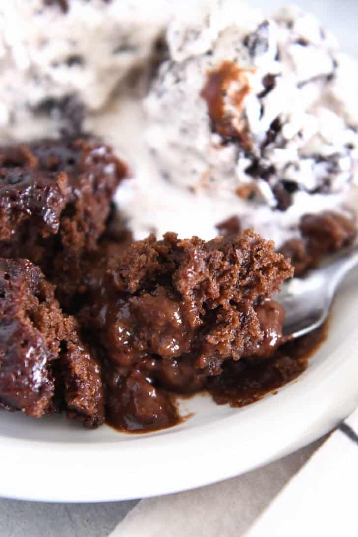 Spoonful of ooey gooey hot fudge pudding cake on white plate.