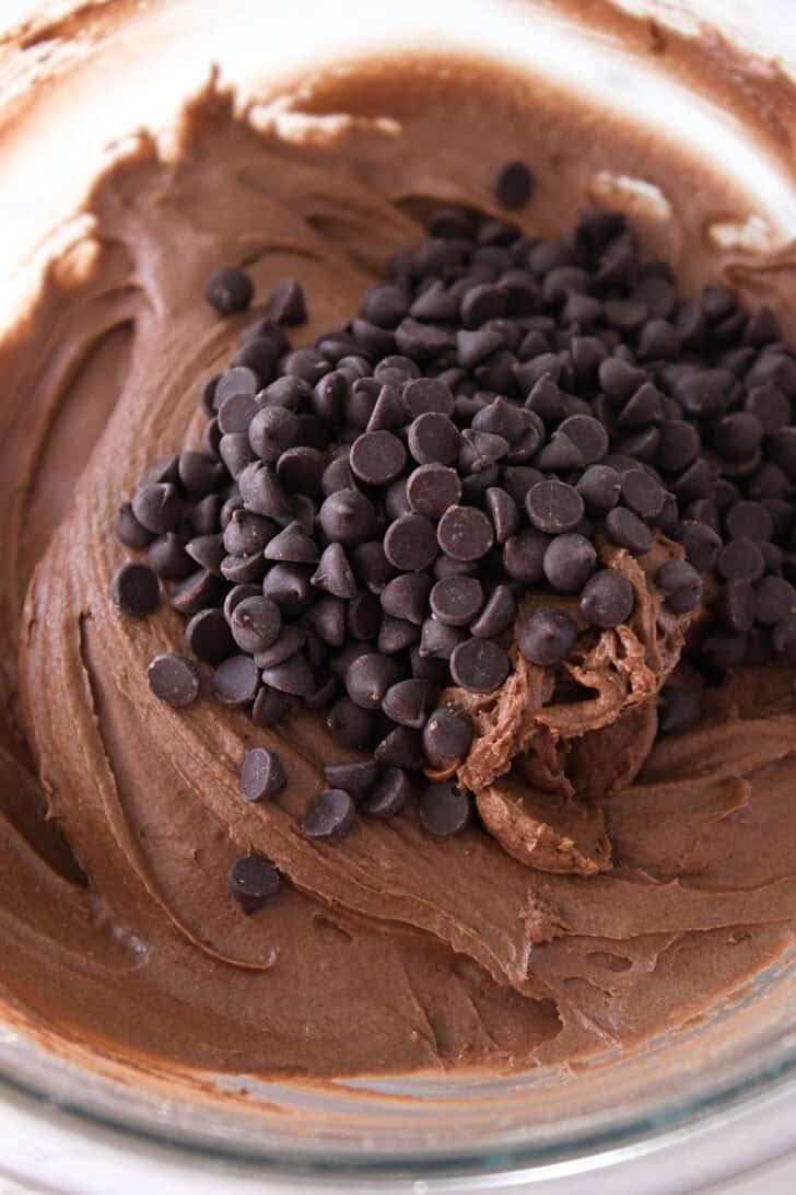 Chocolate chips on top of chocolate cake batter in glass bowl.
