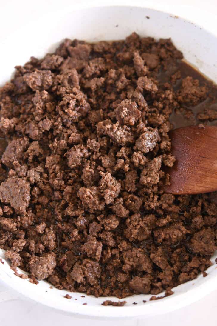 White skillet with ground beef and wooden spoon.