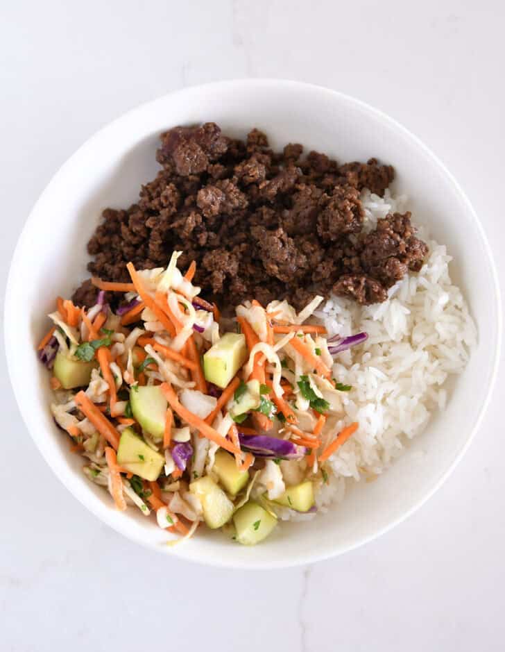 White bowl with rice, slaw, cucumbers, Korean ground beef.
