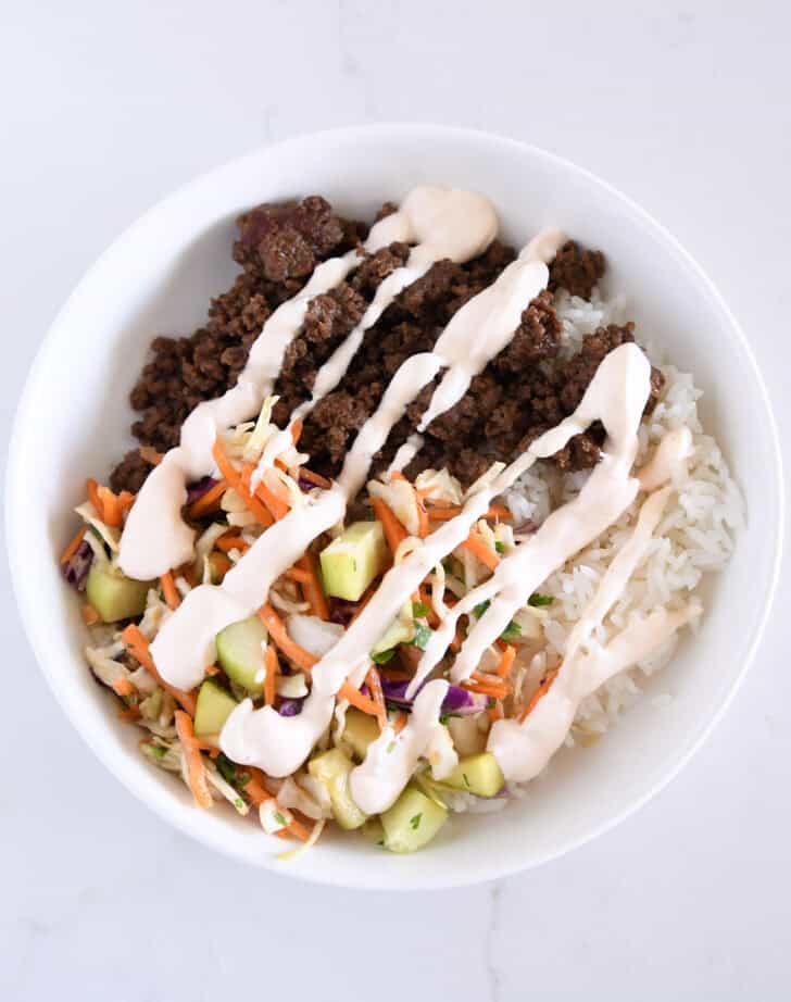 White bowl with rice, slaw, cucumbers, ground beef.