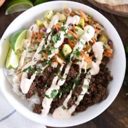 White bowl with rice, Korean beef, slaw, sauce, and lime wedges.