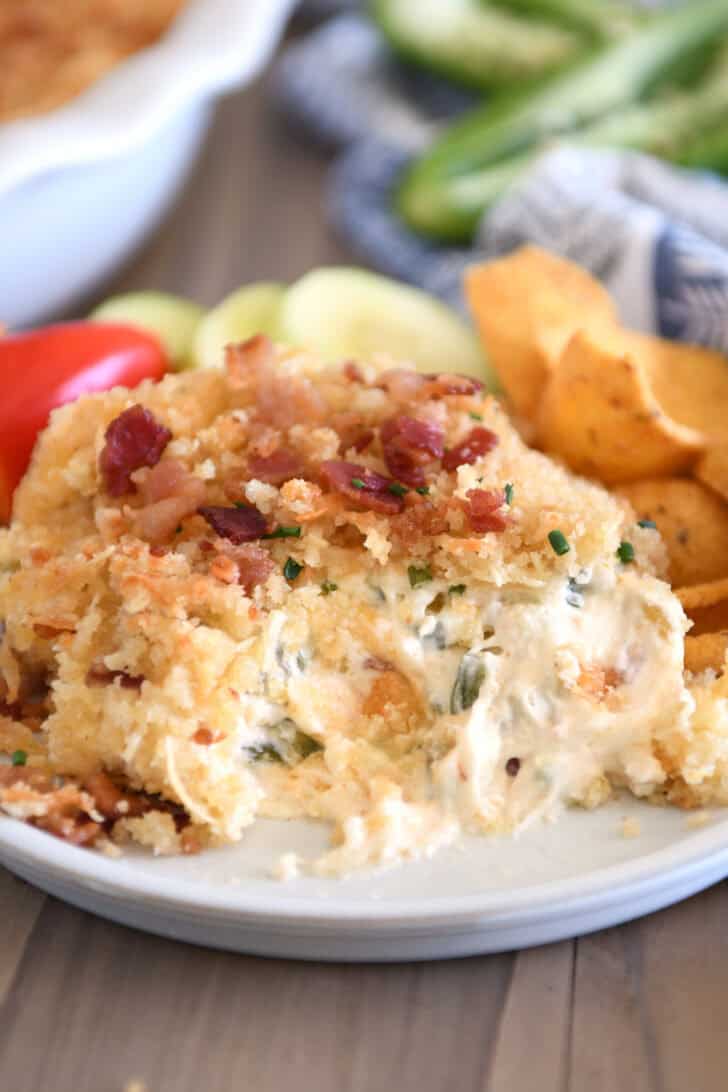 Creamy cheesy bacon dip on gray plate with chips and veggies.