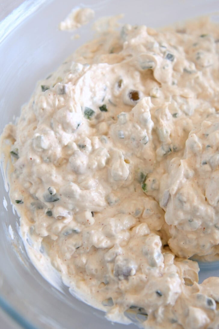 Glass bowl with creamy mixture of jalapenos, mayo, sour cream, green onions.