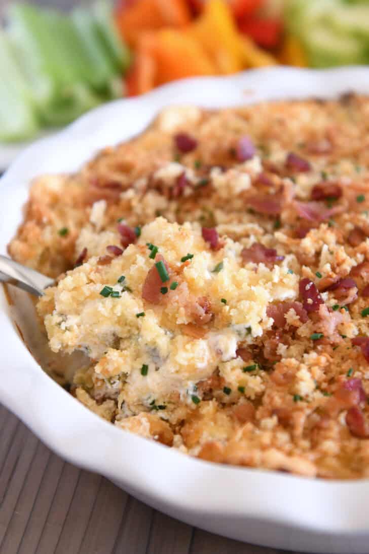 Spoon taking scoop of bacon jalapeno popper dip in white pie plate.