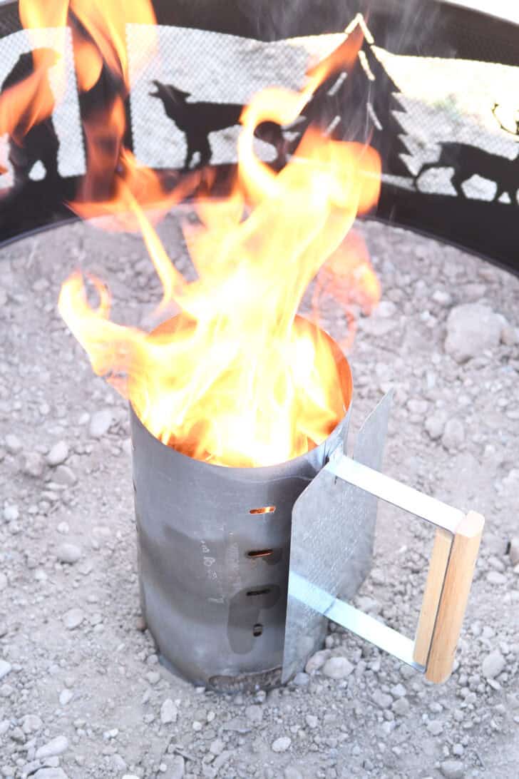 Fire coming out of the top of a chimney starter with briquettes.