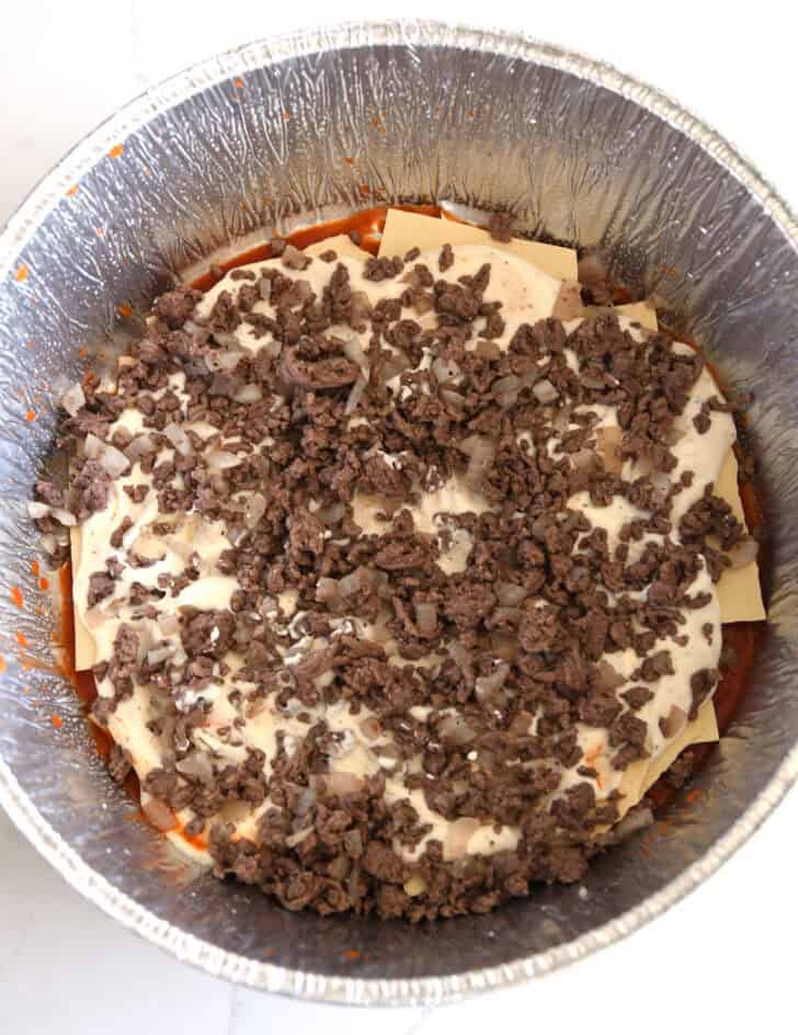 Top down view of ground beef and cooked onions in Dutch oven liner.