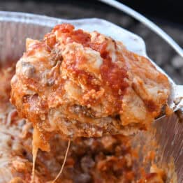 Scooping serving of Dutch oven lasagna with serving spoon.