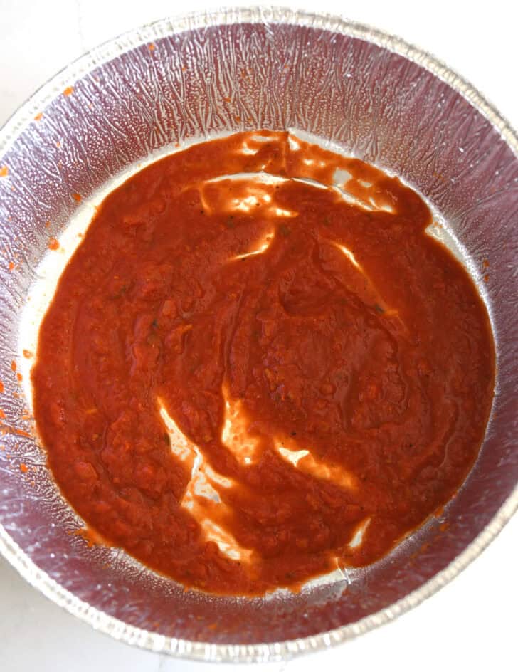 Top down view of pasta sauce spread on bottom of Dutch oven liner.