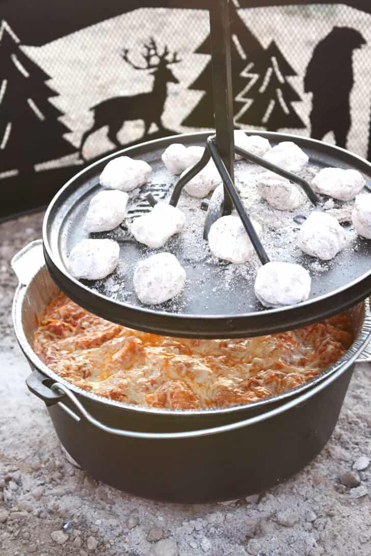 Lifting lid from Dutch oven with coals on top.