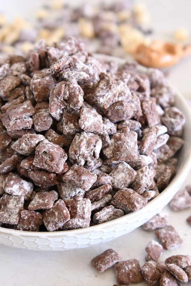 Pile of peanut butter and chocolate puppy chow in white bowl.