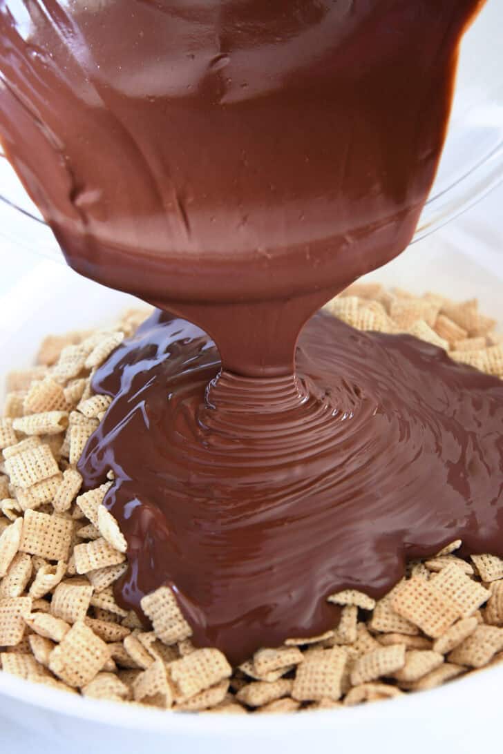 Pouring peanut butter and chocolate mixture over chex cereal.