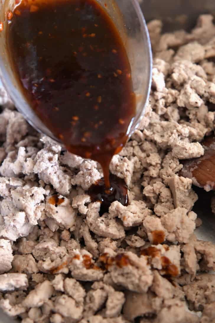 Pouring chili garlic sauce over ground turkey in skillet.
