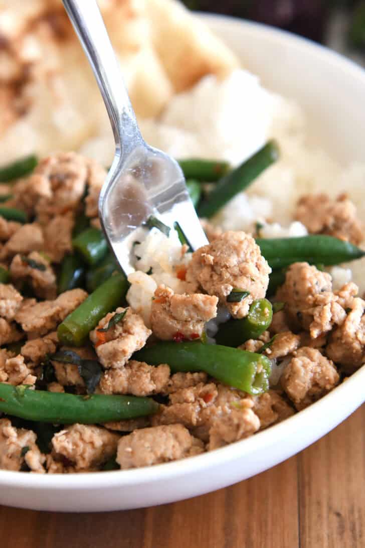 Fork scooping bite of rice, ground turkey, and green beans in white bowl.