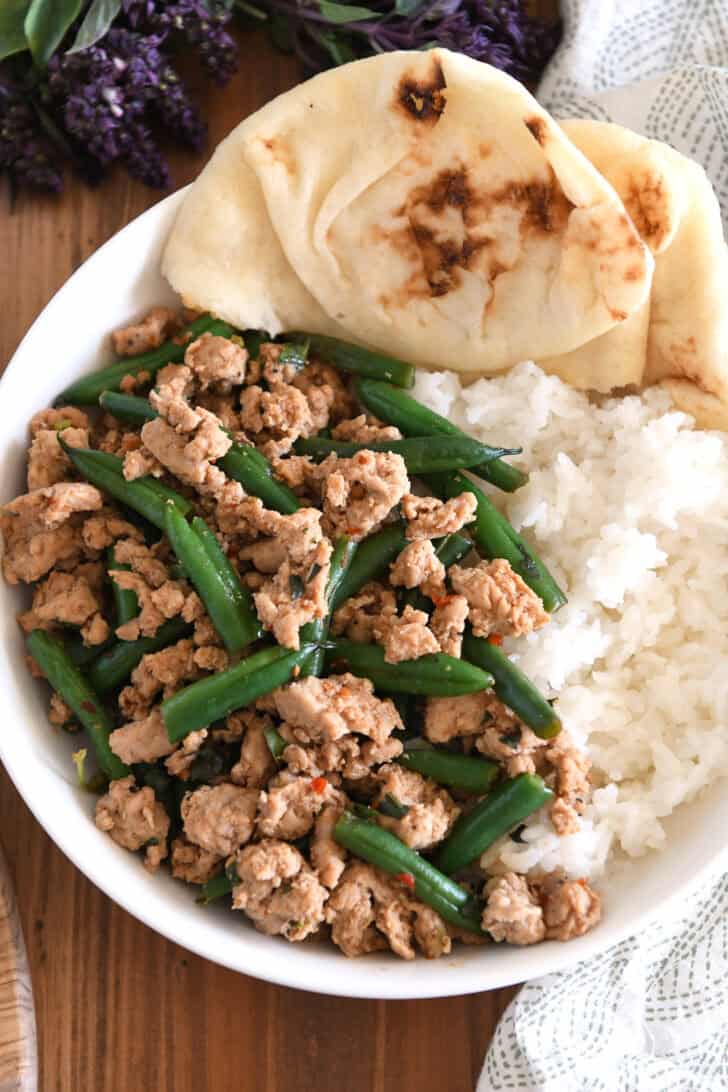Top down view of ground turkey, green beans, rice and naan in white bowl.