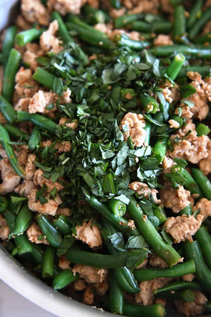 Top down view of Thai basil added to ground turkey and green beans.