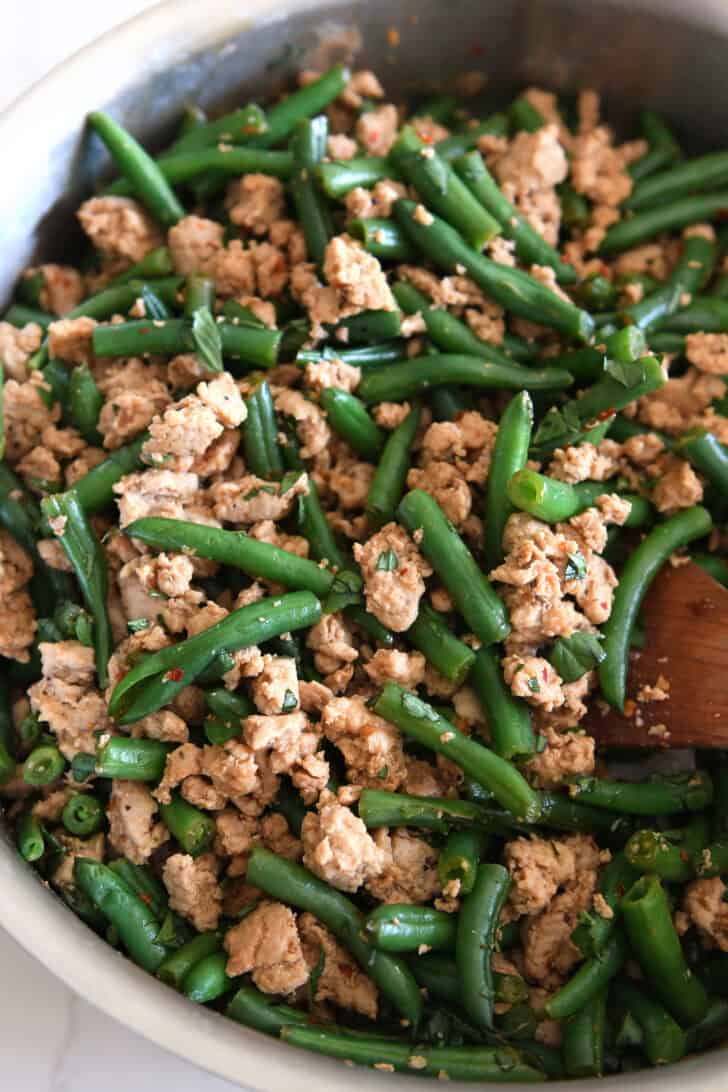 Ground turkey, green beans and seasonings stirred together in stainless skillet.