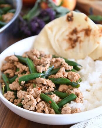 White shallow bowl with rice, naan bread, ground turkey and green beans.