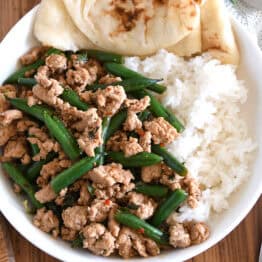 Top down view of ground turkey, green beans, rice and naan bread in white bowl.