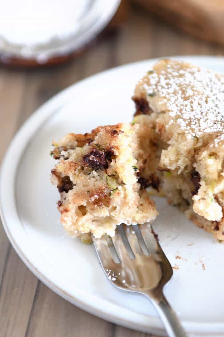 Bite of chocolate chip cake on zucchini cake on fork on gray plate.