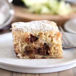 Square of zucchini chocolate chip cake dusted with powdered sugar on gray plate.