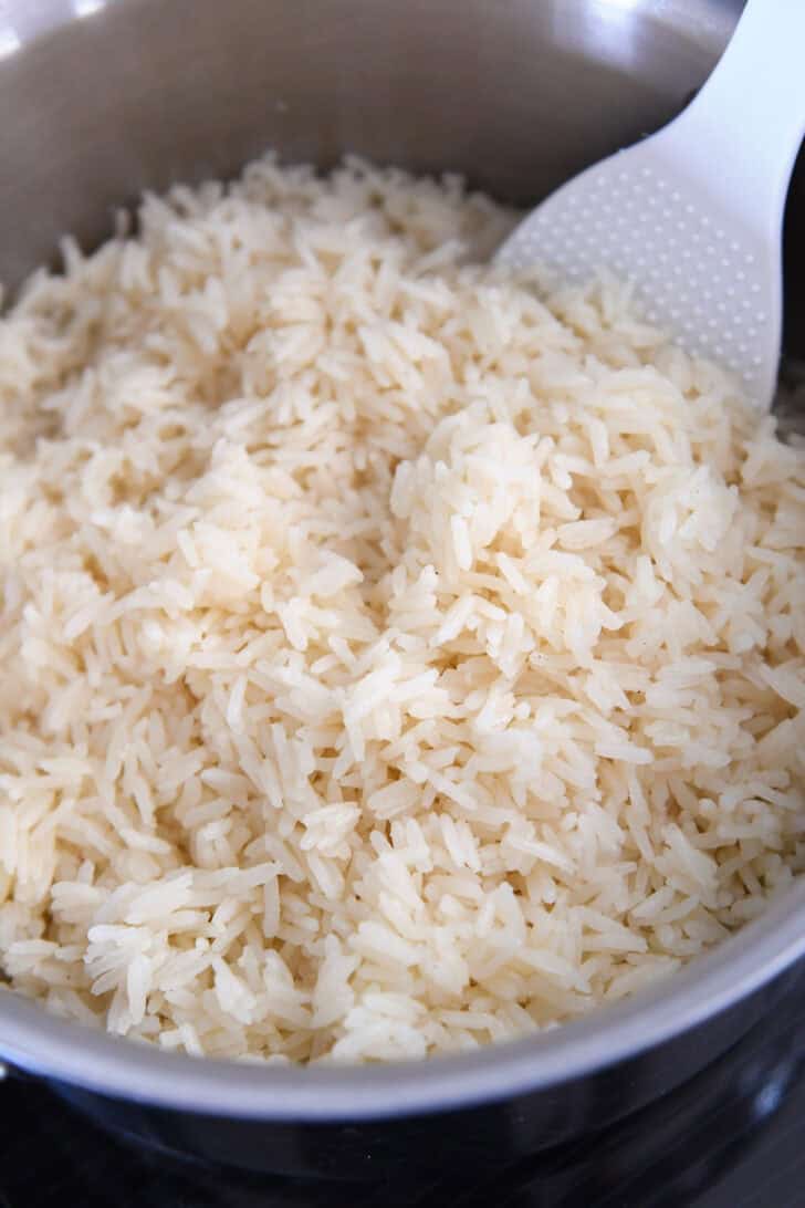 Fluffy cooked rice in stainless pot with white serving spoon.