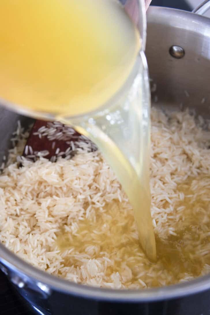 Pouring chicken broth in pan with rice and butter.